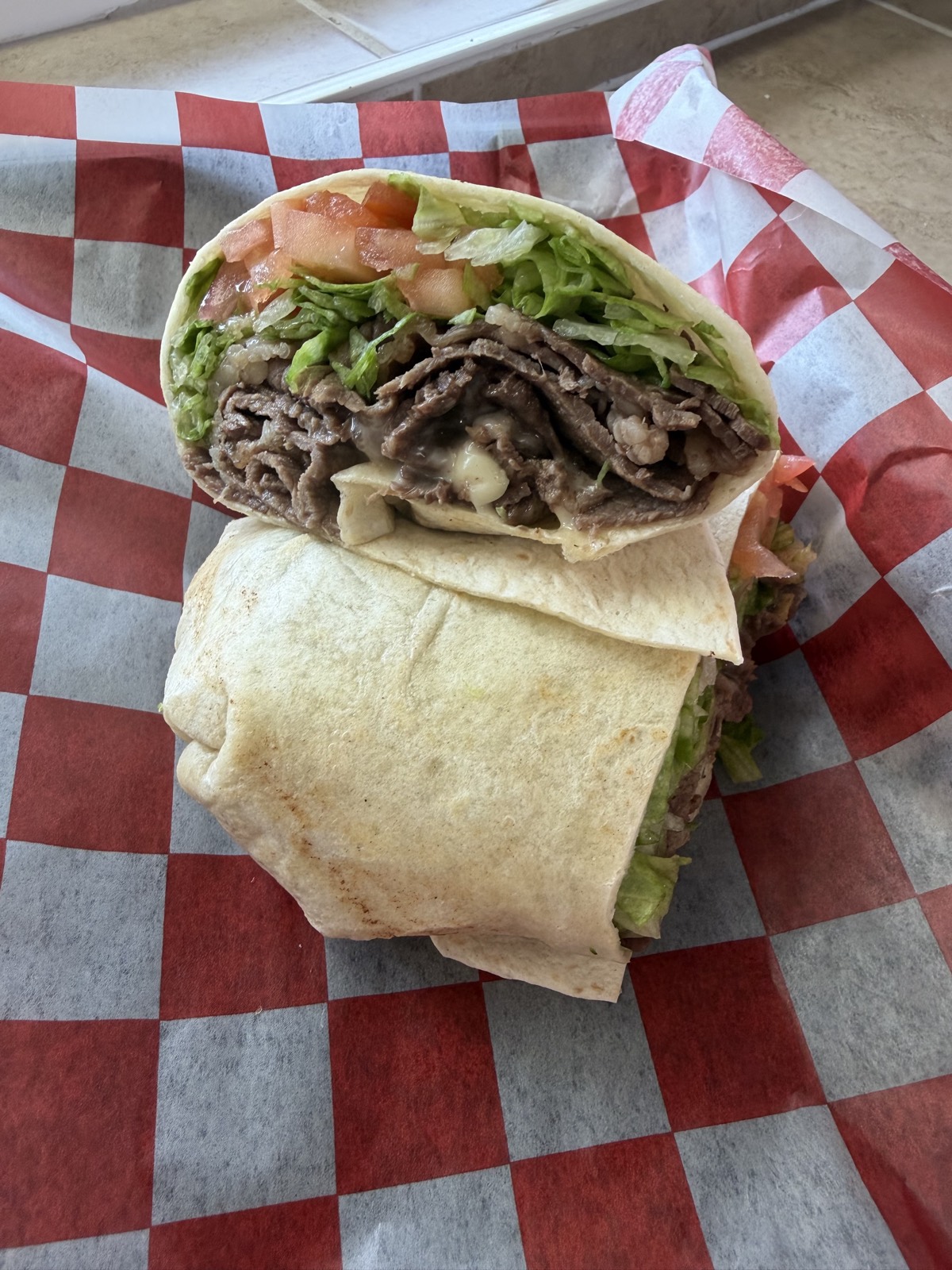Cheesesteak wrap cut open and stacked on checkered paper